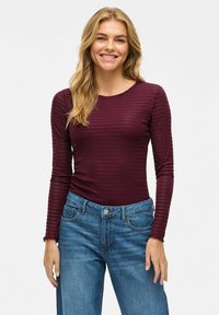 Bordeaux langekragige top met een textuur ribbelpatroon, gecombineerd met lichtblauwe denim jeans met hoge taille. Ronde hals, nauwsluitende pasvorm.