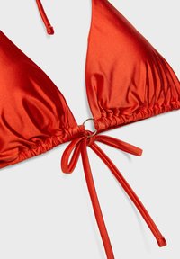 Haut de bikini rouge en forme de triangle avec des liens réglables et un petit anneau en métal reliant les bonnets au centre devant.