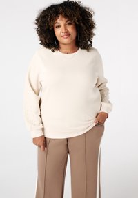 Beige sweatshirt met parelaccenten op de mouwen, ronde halslijn, geribde manchetten, gecombineerd met taupe wijde broek. Vlotte stoftextuur.