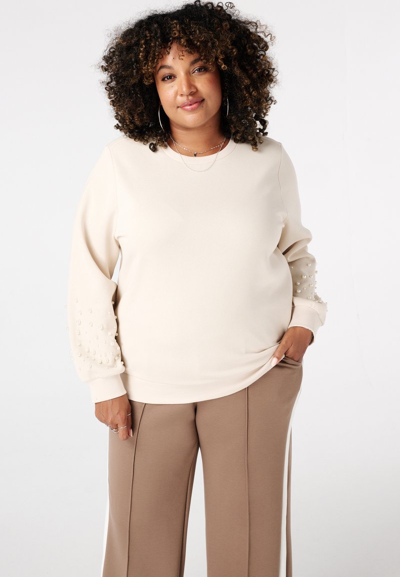 Beige sweatshirt met parelaccenten op de mouwen, ronde halslijn, geribde manchetten, gecombineerd met taupe wijde broek. Vlotte stoftextuur.