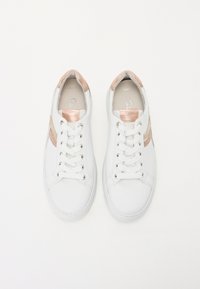 Vita sneakers med metalliska roséguldaccenter, platta snören och en slät läderliknande textur. Har en minimalistisk design med kontrasterande ränder.