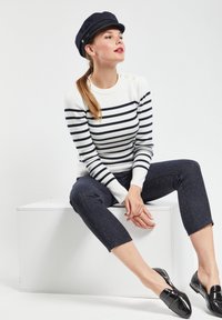 Haut à manches longues rayé en blanc et bleu marine, avec des boutons décoratifs à l'épaule. Assorti à un pantalon cropped bleu marine à motif et des mocassins brillants.