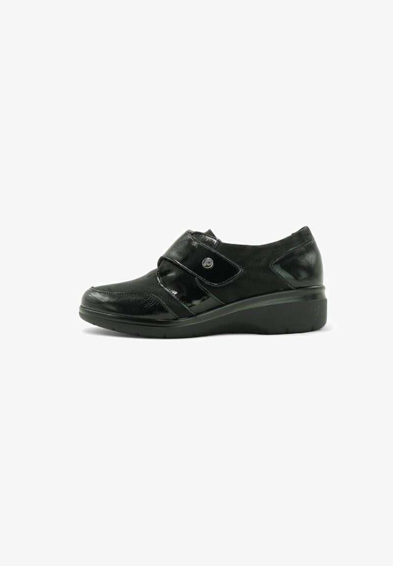 Zapato negro de charol con tacón bajo en cuña, que cuenta con una correa de Velcro en la parte delantera y un diseño texturizado en la parte superior.