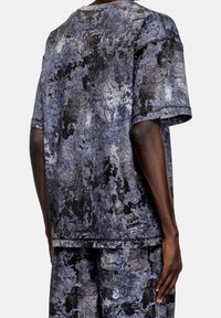 Osoba v odpovídajícím tričku s krátkým rukávem a šortkách s texturovaným abstraktním vzorem v odstínech černé, šedé a modré, viděná zezadu.