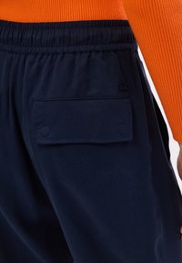 Pantalons de jogging bleu marine avec une taille élastique et deux grandes poches latérales, présentant une texture lisse et un détail de logo de marque discret.