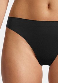 Perizoma nero, senza cuciture, con un design a vita bassa e una texture liscia, caratterizzato da una costruzione minimalista senza dettagli aggiuntivi.