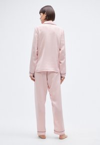 Ensemble de pyjama en satin rose comprenant une veste à col et un pantalon assorti. Détails de passepoil noir aux poignets et à l'ourlet. Texture lisse et coupe décontractée.