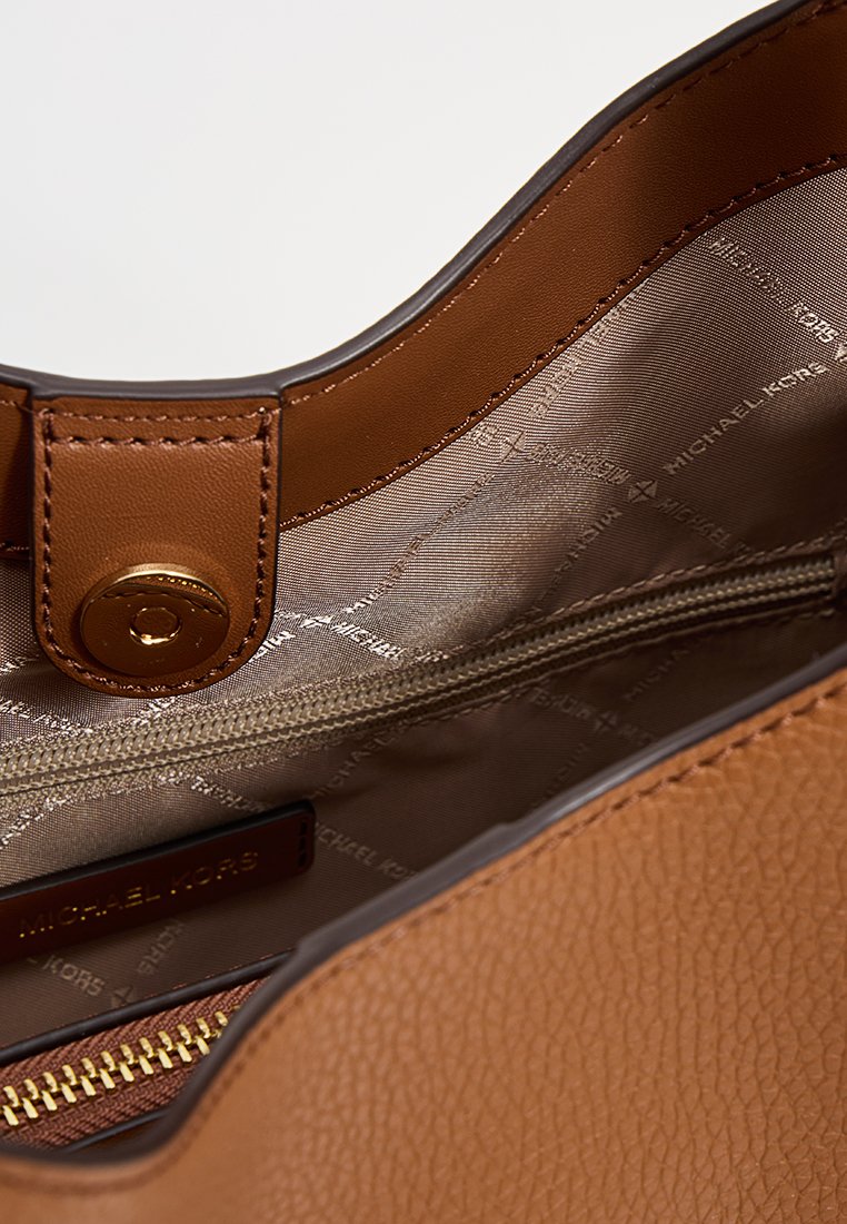 Interieur van een bruin lederen handtas met een gladden stofvoering. Beschikt over een ritsvak en een magnetische drukknoopsluiting. Met gouden hardwareaccenten.