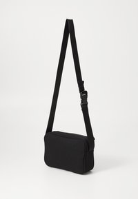 Black shoulder bag with a rectangular shape, made of textured fabric. Features an adjustable strap and a zippered top closure.