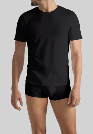 Schwarzes T-Shirt mit kurzen Ärmeln aus glattem Stoff, mit rundem Ausschnitt und nahtlosen Schultern, kombiniert mit schwarzen figurbetonten Shorts.