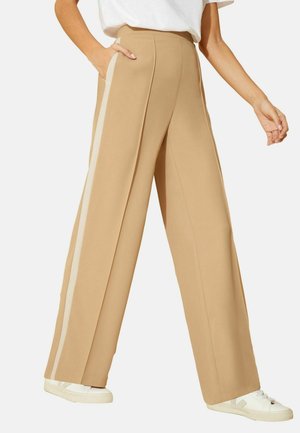 Pantalons larges beige avec poches latérales, présentant une bande blanche contrastante le long de la couture extérieure et un tissu lisse et texturé.