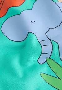 Bunter Stoff mit blauem Elefantendesign vor grünem Hintergrund, begleitet von orangenen und grünen Blattakzenten.