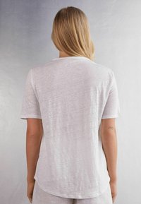 Hvid linned t-shirt med en afslappet pasform, korte ærmer og en rund fald. Stoffet har en subtil tekstur og en let gennemsigtighed.
