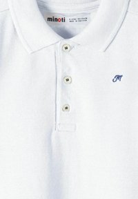 Camisa polo blanca con una textura suave, que presenta un cierre de tres botones y un pequeño logo bordado en azul en el lado izquierdo del pecho.