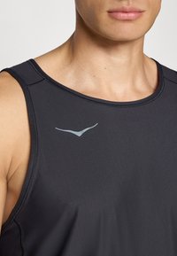 Mann in einem ärmellosen schwarzen Sportshirt mit einem reflektierenden, vogelähnlichen Logo auf der Brust, das den Hals und den unteren Teil des Gesichts zeigt.