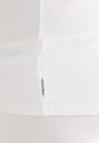 Hvit bomull T-skjorte med myk tekstur og rett snitt, med en liten vevd "Calvin Klein" etikett på sidesømmen.