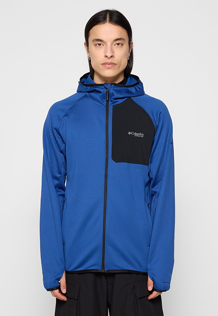 Veste à capuche bleue en tissu texturé, poche poitrine noire, fermeture éclair intégrale et manches longues ; présente un logo sur le côté gauche.