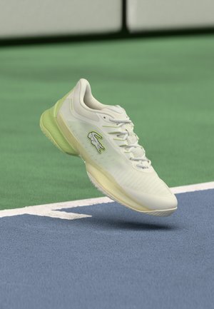 Lacoste tennis shoe featuring a white mesh upper with light green accents, a textured sole, and a prominent logo on the side.