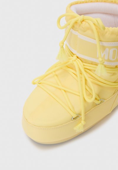 Yellow winter boot with a smooth fabric upper, round toe, prominent lacing system, front tassels, and branding on the side.