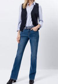 Granatowa kamizelka na jasnoniebieskiej koszuli w paski, zestawiona z niebieskimi dżinsami i wzorzystym paskiem. Całość dopełniają czarne botki.