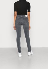 Šedé slim džíny s vysokým pasem, pěti kapsami a bílou štítkem vzadu. Nosič obutý v bílých sportovních botách. Hladká směsová tkanina z bavlny.