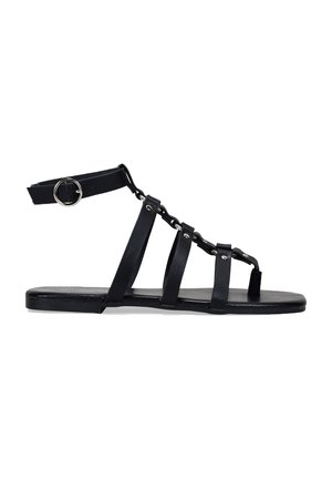 Sandalias planas negras con múltiples correas y un acento de cadena. Hechas de material sintético con una textura suave y un diseño de punta abierta.