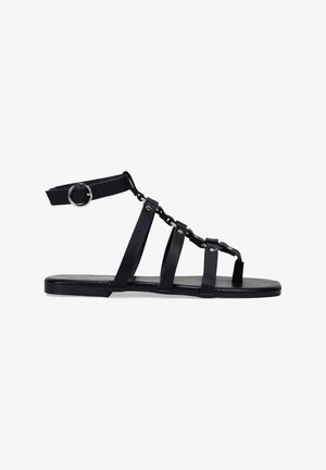 Sandalias planas negras con múltiples correas y un acento de cadena. Hechas de material sintético con una textura suave y un diseño de punta abierta.