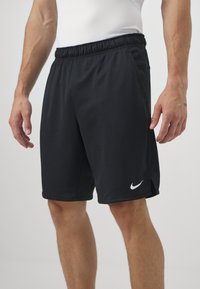 Černé sportovní šortky vyrobené z lehké tkaniny s elastickým pasem, vybavené bočními kapsami a bílým logem Nike na lemování.