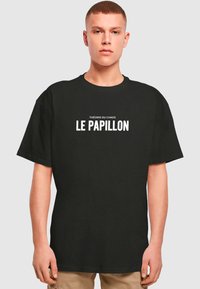 Sort bomulds t-shirt med korte ærmer, med hvid tekst der står "THÉORIE DU CHAOS LE PAPILLON." Klassisk, løst fit design.