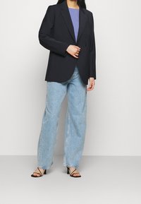 Svart blazer med en knapp, bärs över en lila topp, kombinerat med ljusblå vida jeans och svarta remsandaler.