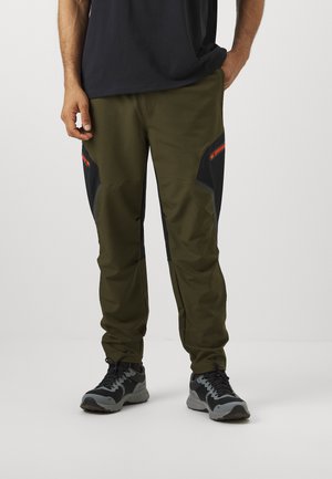 Olive green pants with black accents, featuring zippered pockets and a tapered fit. Made from lightweight, stretchy fabric for comfort.
