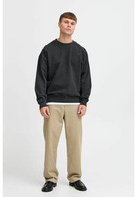 Mørkegrå genser med rund hals, løs passform, ribbestrikkede mansjetter og nederkant, brukt over en hvit T-skjorte. Beige bukser og svarte sko.