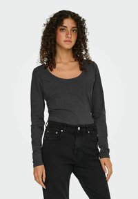 Langarm, scoop-neck top van donkergrijze stof, gecombineerd met high-waisted zwarte jeans met knoopaccenten en zakken.