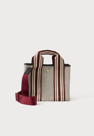 Malá béžová látková taška s širokými vínovými a béžovými pruhovanými uchy a odnímatelným vínovým ramenním popruhem na bílém pozadí.