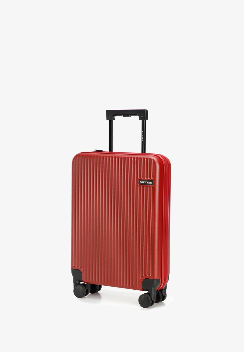 Valise rigide rouge avec des rainures verticales, poignée extensible noire et quatre roues noires pour la mobilité. Présente un logo de marque.