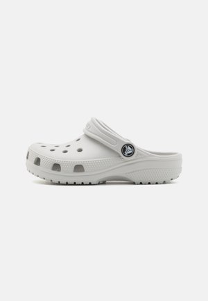 Des crocs blancs avec un bout fermé, un design léger, des trous de ventilation et une sangle à l'arrière. Semelle texturée pour une meilleure adhérence. Accent logo noir.