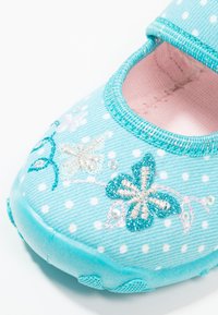 Lichtblauwe stoffen schoen met witte stippen, geborduurde bloemen in roze en groen. Heeft een elastische band en een rubberen zool met textuur.