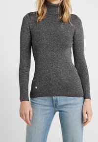 Svart rullkragetröja med ribbat mönster och strukturerad design med silverfläckar, långa ärmar och en figurnära silhuett.