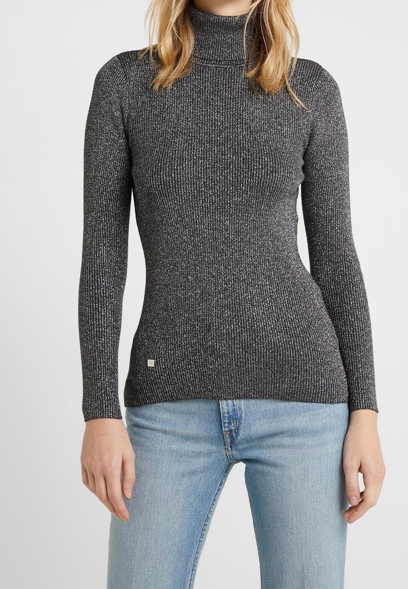 Svart rullkragetröja med ribbat mönster och strukturerad design med silverfläckar, långa ärmar och en figurnära silhuett.