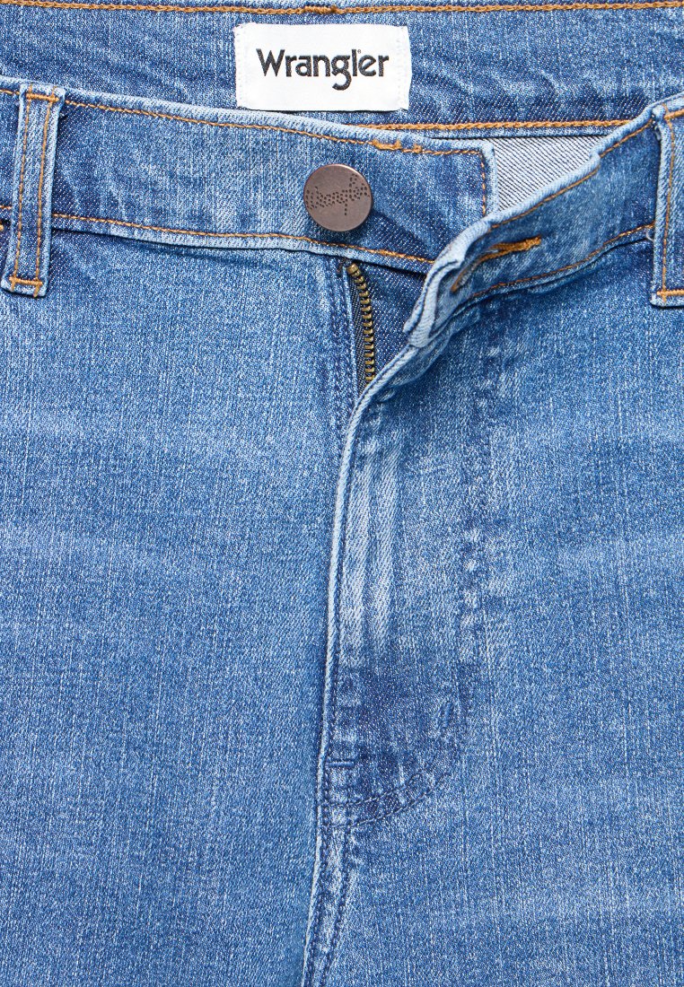 Niebieskie dżinsy z zamkiem błyskawicznym, etykieta Wrangler i czerwonobrązowy metalowy guzik; wyróżniają się pomarańczowymi szwami oraz tradycyjnym pięciopakowym wzorem.