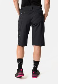 Schwarze Shorts aus leichtem Material, mit zwei seitlichen Reißverschlusstaschen, verstellbarem Bund und glattem Stoff. Schwarze Schuhe mit rosa Akzenten.