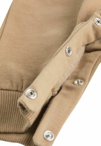 Sezione in cotone beige con bottoni a pressione. Presenta una texture a coste e una finitura in tessuto liscia con dettagli in metallo argentato.