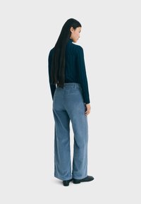 Blauwe corduroy wijde broek met verticale strepen, gecombineerd met een donkerblauwe gestructureerde trui. Soepele stof met duidelijke ribbeldetails.