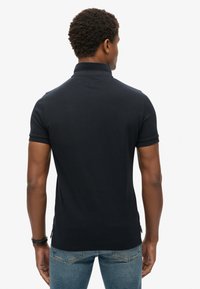 Zwarte polo shirt met een getailleerd ontwerp, korte mouwen en een kraag. Gemaakt van gladde stof, met zijsplitten aan de onderkant voor gemak in beweging.