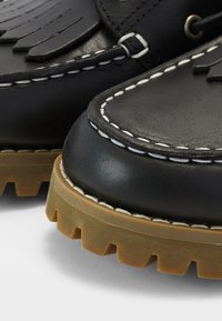 Gros plan de bottes en cuir noir avec coutures blanches et semelles épaisses en caoutchouc marron à crampons profonds.