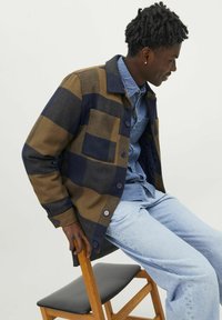 Ruskea ja tummansininen ruudullinen takki, jossa on kauluspaita ja napitus, kahdella etupussilla ja sileällä kankaalla. Vapaa-ajan tyyli.