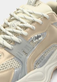 Bézs és szürke sportcipők hálós betétekkel, párnázott nyelvvel és jellegzetes logó részletekkel. A világos színű fűzők emelik ki a dizájnt.