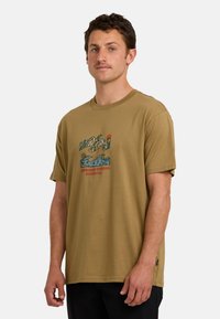 Koszulka z krótkim rękawem w oliwkowym kolorze, wykonana z bawełny. Posiada graficzny wzór przedstawiający góry, fale i palmy w kolorach niebieskim i czerwonym.