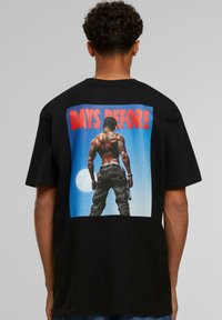 Sort bomulds-T-shirt med et ryggrafik af en figur mod en blå baggrund med teksten "DAYS BEFORE" i rød. Korte ærmer, afslappet pasform.