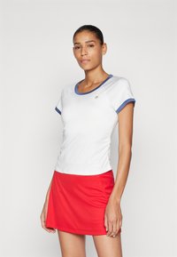 Hvit atletisk topp med blå trim, kombinert med et rødt skjørt. Har korte ermer og rund halslinje. Glatt tekstur og tettsittende design.